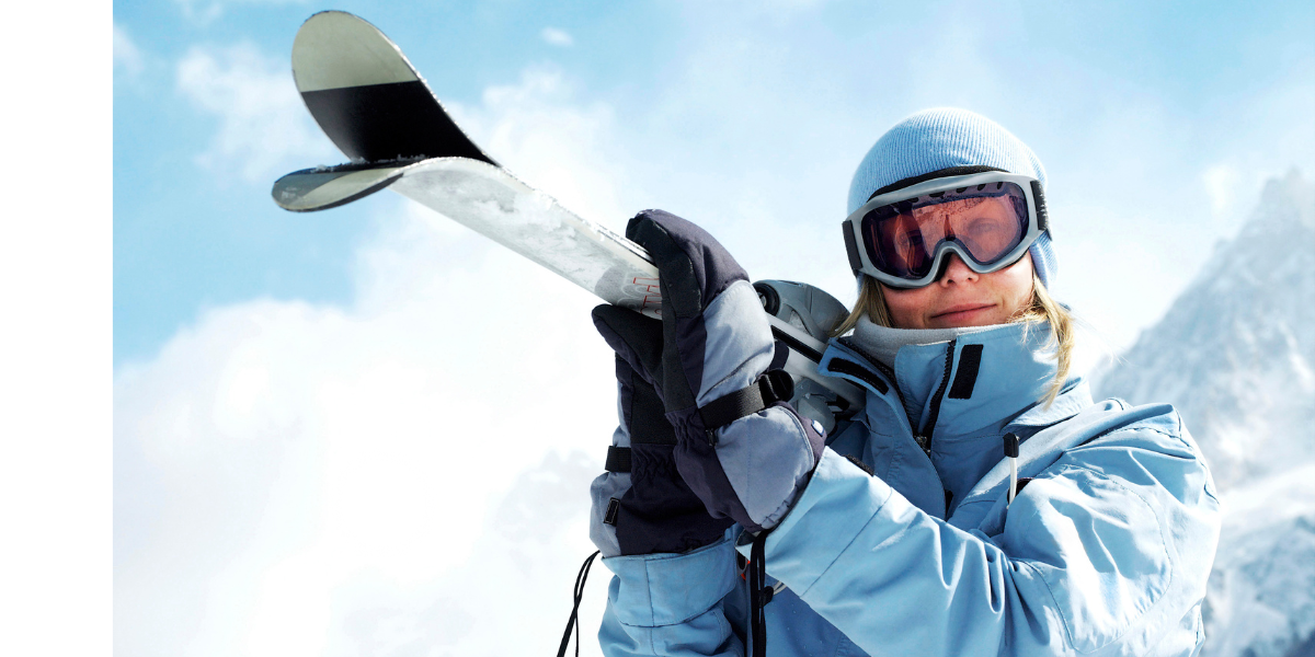 Person wearing a blue outdoor skiing jacket holding skis in snowy mountains