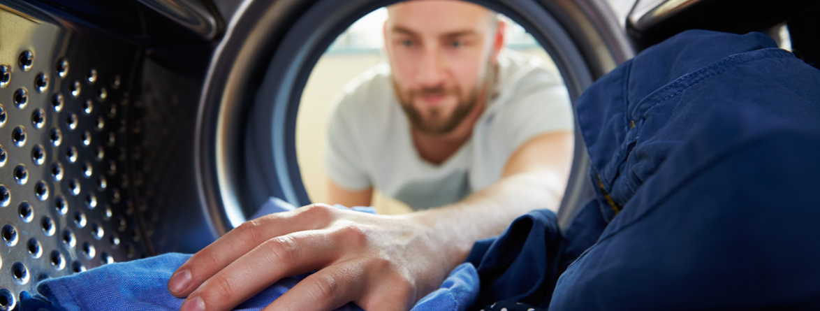 Man loading water-repellent outdoor jacket into washing machine for proper garment care
